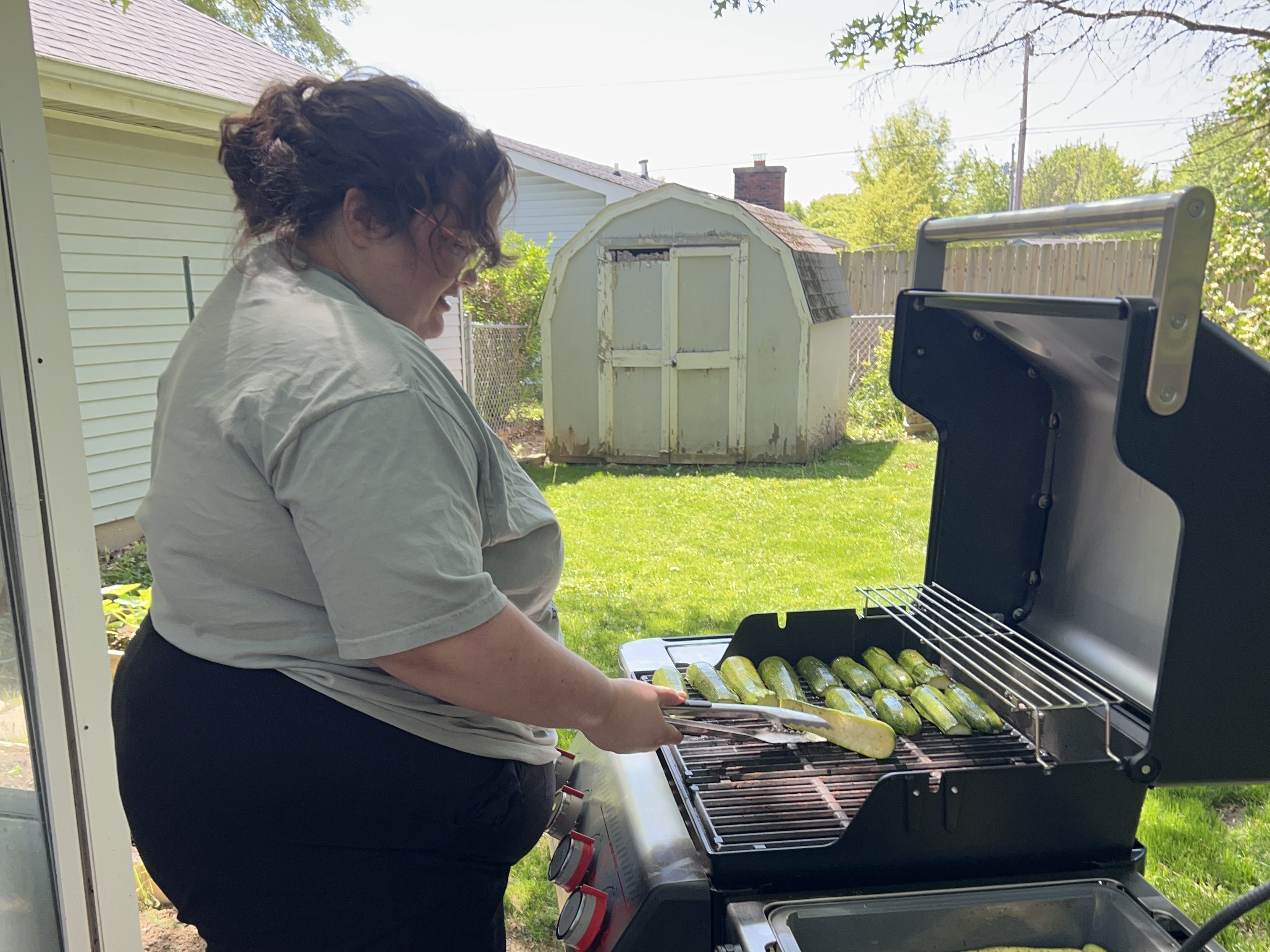 The author standing at a grill in her backyard making zucchini. 